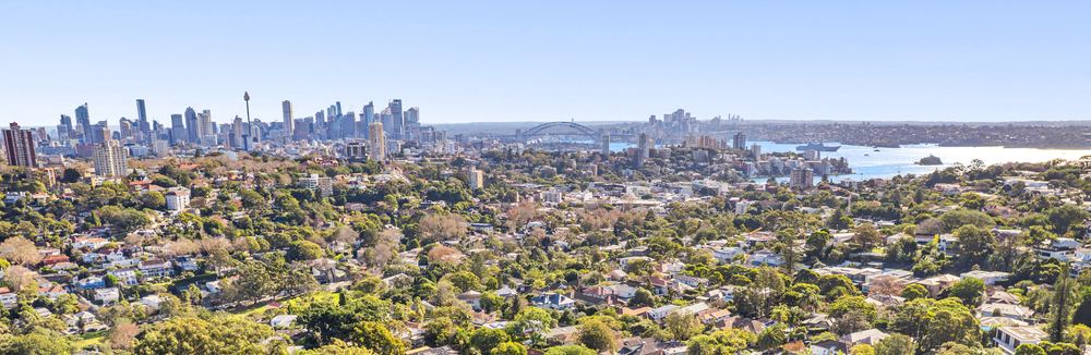 Aerial view over the leafy rooftops of Bellevue Hill towards the Sydney city skyline and the harbour