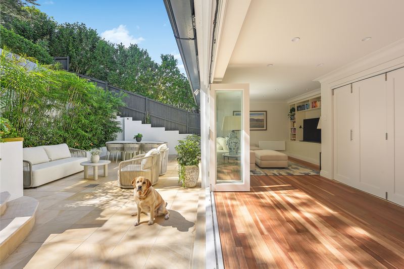 Open-plan living room with timber floors, bi-fold doors fully open to a paved terrace with outdoor lounges