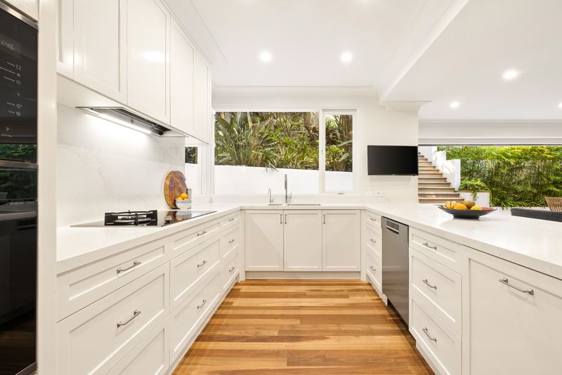 Kitchen with white cabinetry, stone benchtops, induction cooktop and a window to the garden
