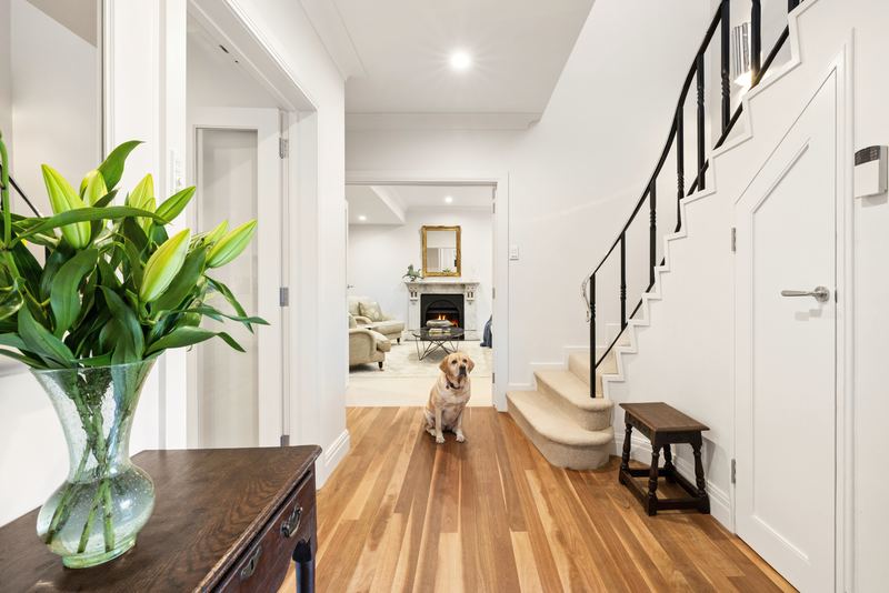 Entry hall with timber floors and a staircase, looking through to the lounge fireplace